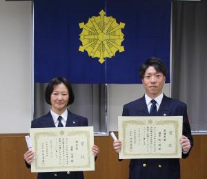 表彰授与式終了後、最優秀賞の藤原副士長（右側）と優秀賞の荻野消防士（左）が賞状を持ち、立って並んでいる写真。